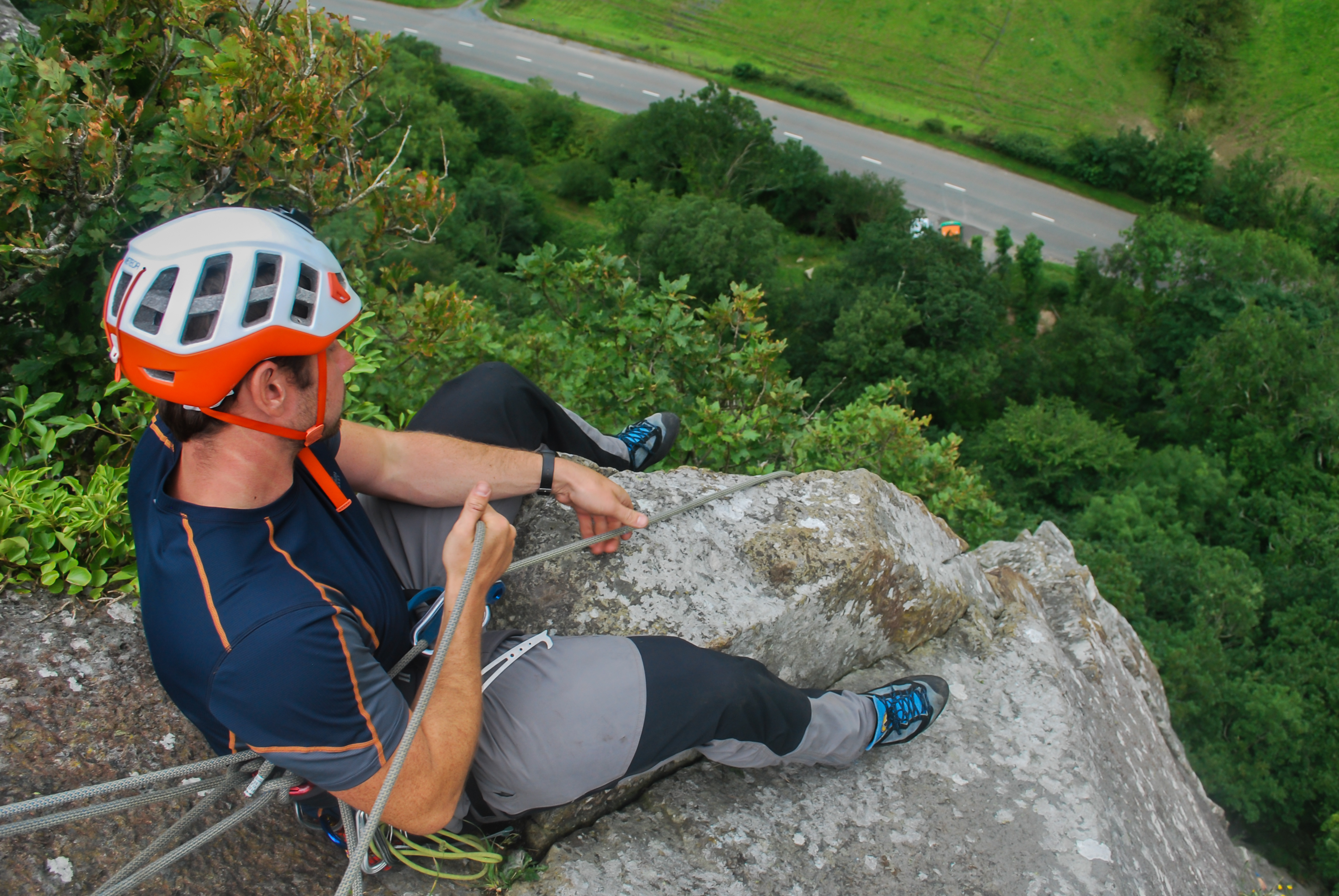 Man in blue shirt belaying a friend who is out of sight of the shot on a rock face | Higher Climbing – Wales mountain climbing courses and guided adventures for beginners and experienced climbers
